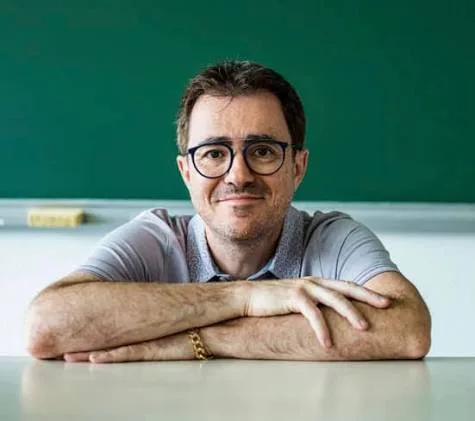 Yvan Monka, professeur de mathématiques, attablé devant un tableau vert